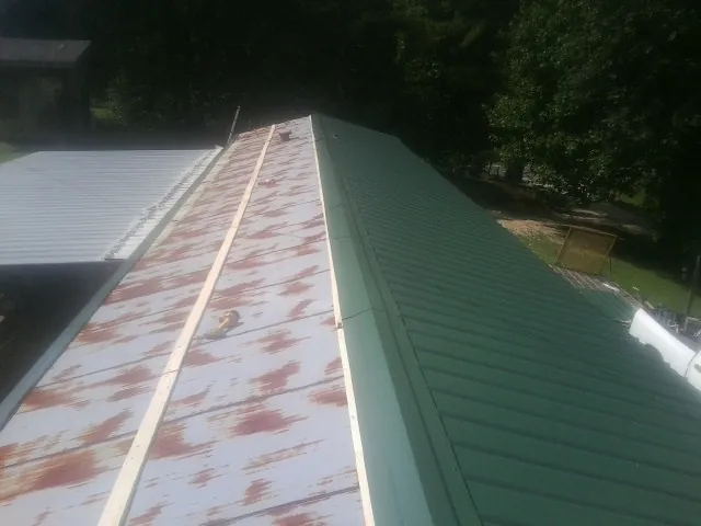 Old rusted panels beside newly installed green metal roofing — Wind Damage Roof Repair by Roofing Brothers in Myakka City