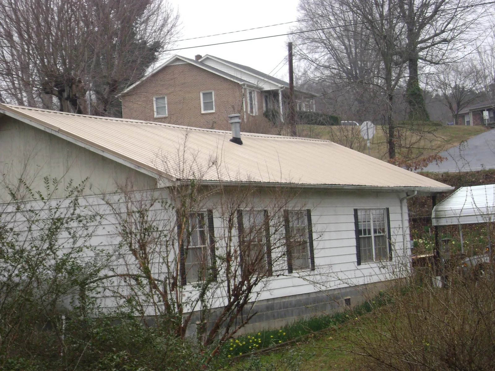 Tan metal roof on a white sided house set into a hillside — Commercial Roofing by Roofing Brothers in Myakka City